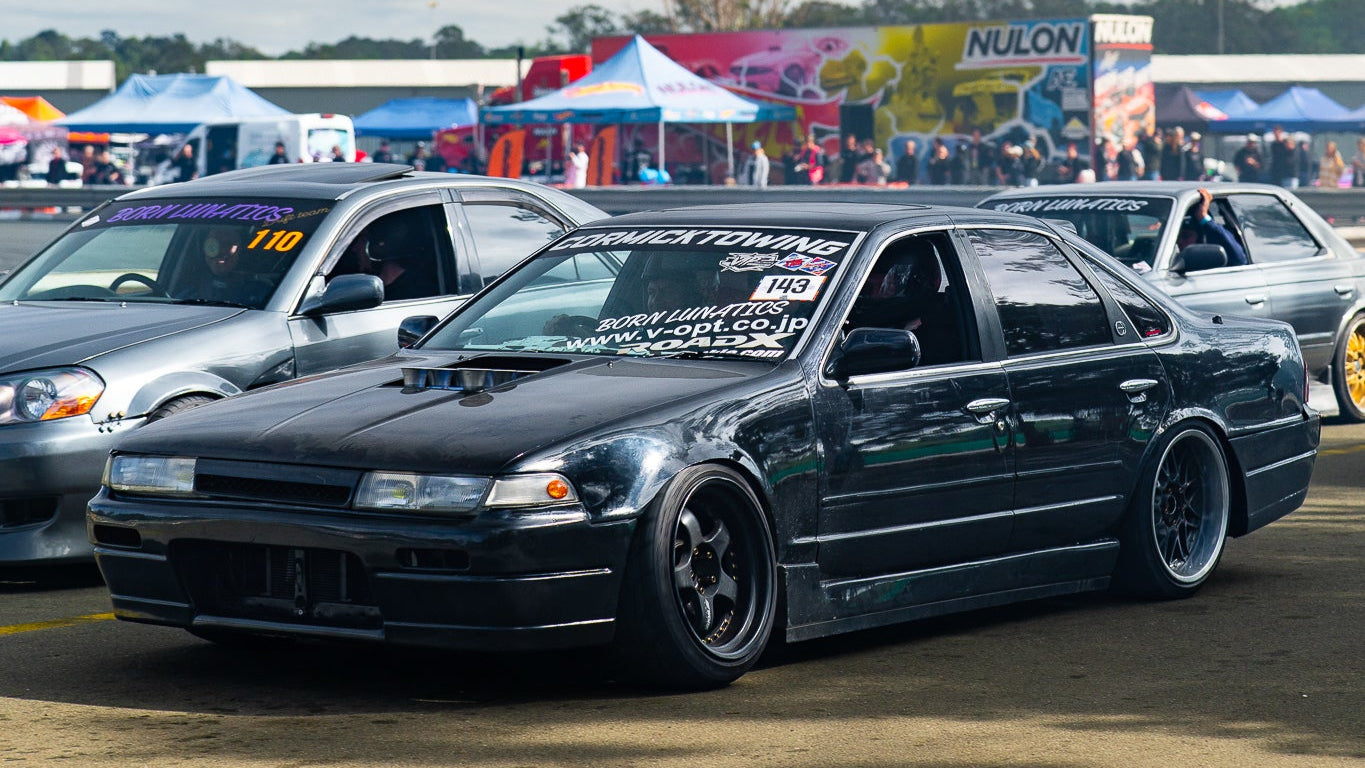 Black car on a track with tents and people in the background